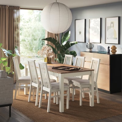 Modern white & wood dining set with table, chairs, pendant light, plants, art, & sideboard.