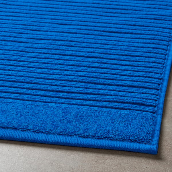 Bright blue, thick cotton bath mat with high absorption, laid on grey floor.