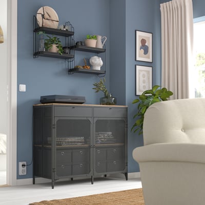Black metal shelf with plants, decor, and electronics, fitting in room corner next to beige armchair.