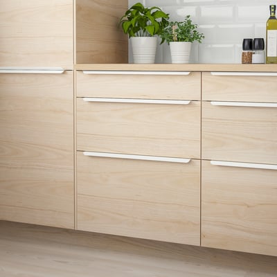 ASKERSUND light ash wood kitchen cabinet. Modern, smooth front with silver handles. Tall, narrow design, wider than pots.