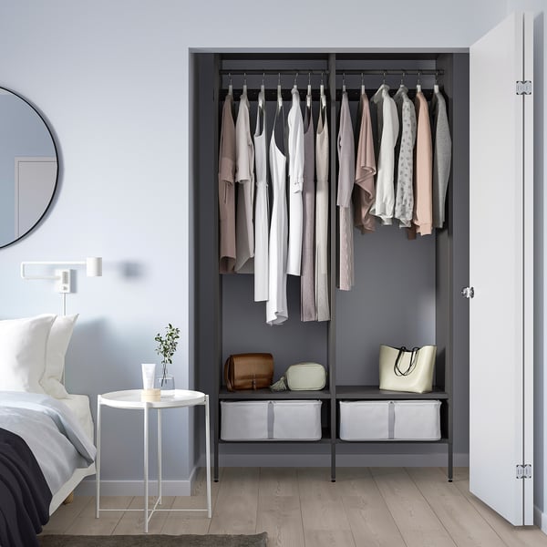 Modern AURDAL black closet with clothes, shelves, and table with plant beside bed.
