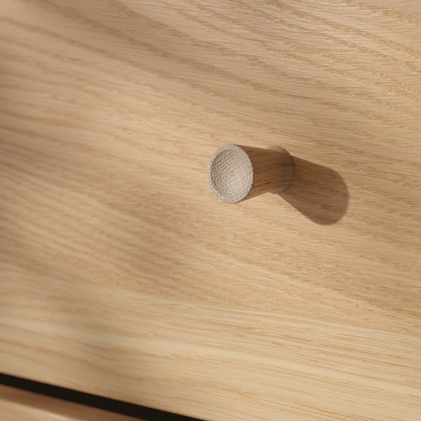 Close-up of wooden drawer with a round, knitted handle. Natural wood grain texture visible.