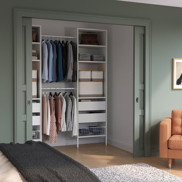 White AURDAL closet organiser with shelves, drawers, rails, near wall and leather chair.