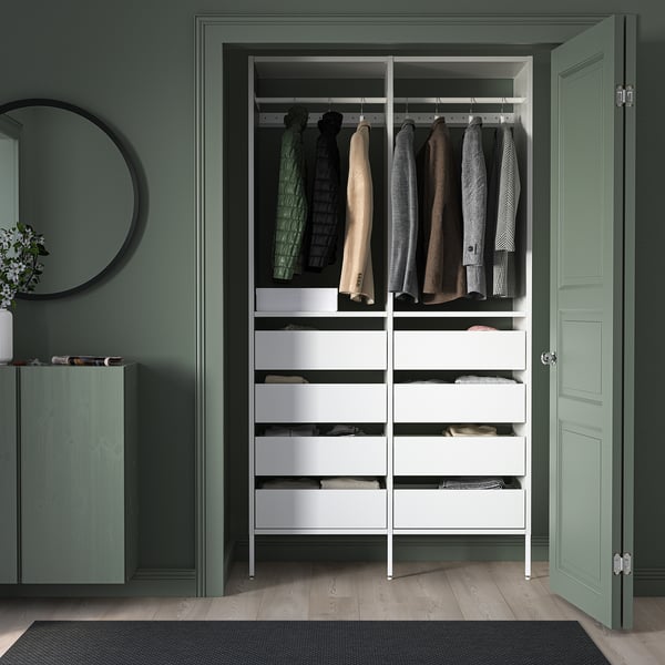 White closet system with drawers, hangers, against green wall, mirror, plant, open door.