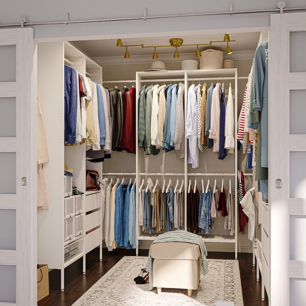 White closet system with clothes, shelves, drawers, and ottoman.