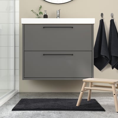 Modern bathroom with BACKMÅRA grey bath mat, sleek vanity, hanging towels, and wooden stool. Mats size complements vanity and stool.