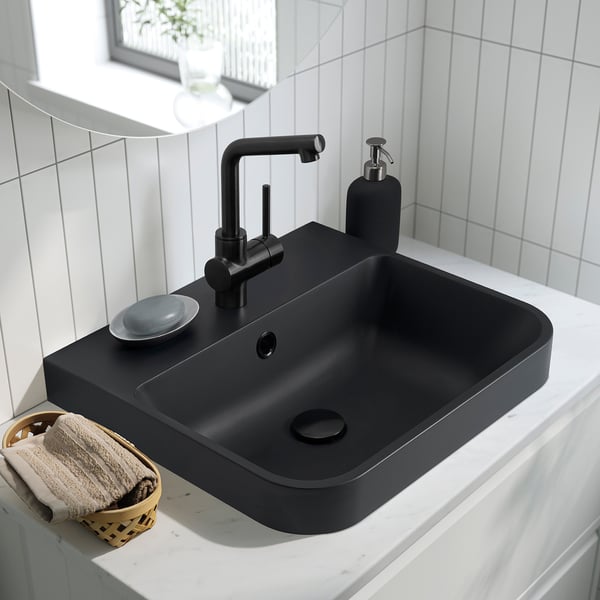 Black semi-recessed washbasin on countertop with modern tap, soap dispenser, and towel basket.