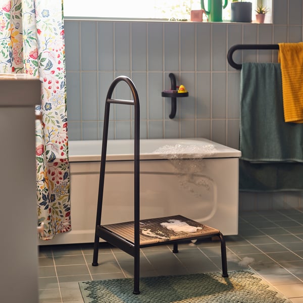 Modern grey bathroom with white bathtub, black stool, floral curtain, and yellow towel.