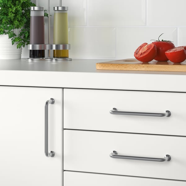 Modern kitchen with white cabinets and stainless steel handles. Countertop a cutting board with sliced tomatoes and condiment dispensers.