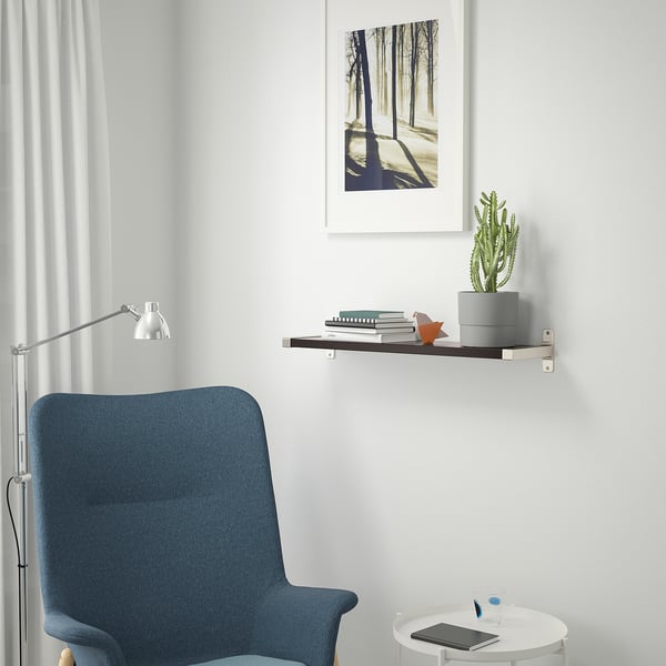 A minimalist reading nook with shelf, plant, books, figurine, chair, lamp, and table with tablet.