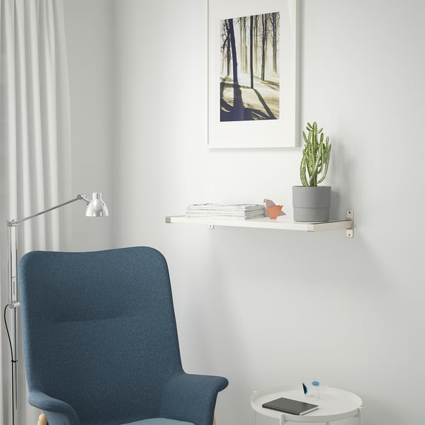 Modern workspace with blue office chair, round table, and shelf with plant and art.