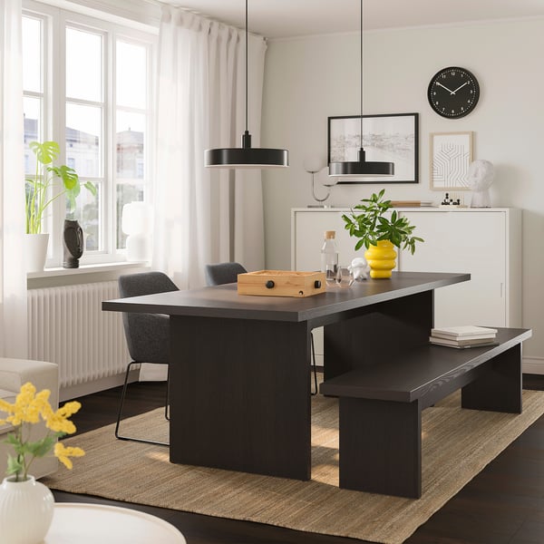 Modern dining setup with BERGSHYTTAN dark wood table, grey chairs, yellow vase, green plant, and pendant light.