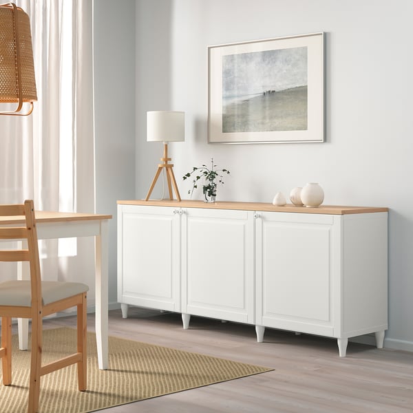 Modern living room with BESTÅ sideboard, lamp, plant, beach print, white chair.