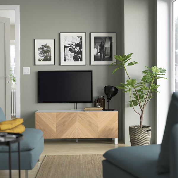 Modern living room with BESTÅ tv bench, blue couch, and wall art. The wooden tv bench has a flat screen tv, lamp, and plant.