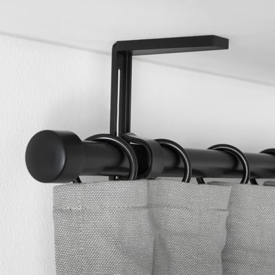 Black adjustable curtain rod bracket holding grey curtains, mounted on white wall.