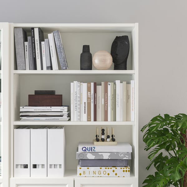 White BILLY bookshelf with multiple shelves holding books and decorative items, including a wooden box, vases, and game boxes.