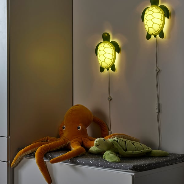 Three glowing turtle night-lights mounted on a wall above a baby changing table with stuffed sea creature toys, including an orange octopus, on it.