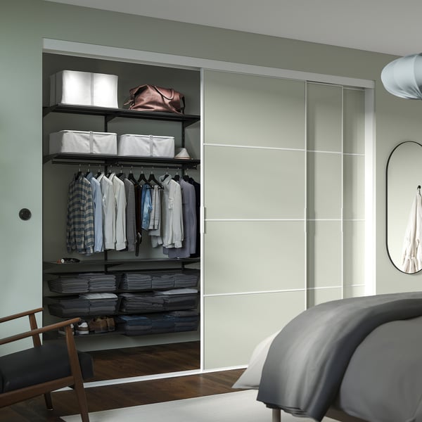 Modern closet with clothes, baskets, and bed. Open shelves with white bins and hanging shirts.