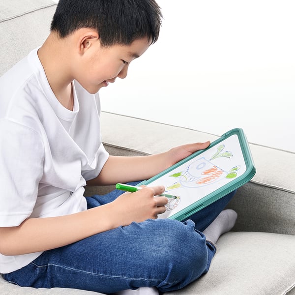 A child draws on a magnetic whiteboard attached to a multi-functional holder that props up a tablet.
