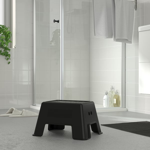 Small black plastic step stool near bathroom shower. Suitable for kids and adults. Non-slip top and bottom.