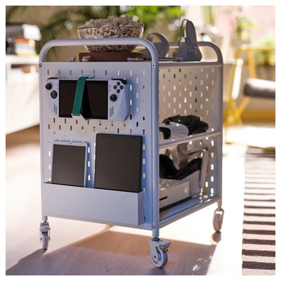 BRÄNNBOLL gaming cart, grey, metal, organised gaming gear, multiple compartments, mobile, compact, on wooden floor, striped rug nearby.