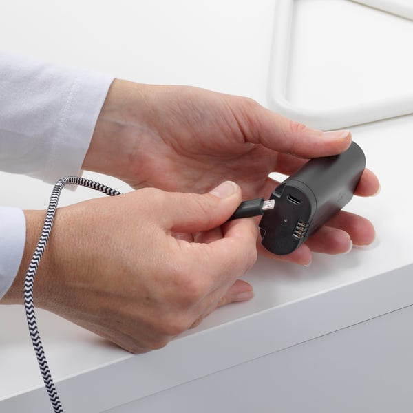 Hands plug a black charging device into a usb port, demonstrating the BRAUNIT battery packs charging function.