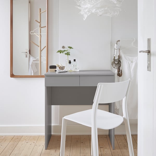 Minimalist desk area with grey BRIMNES desk, white chair, mirror, and decorations. Desk is smaller than the mirror and chair.