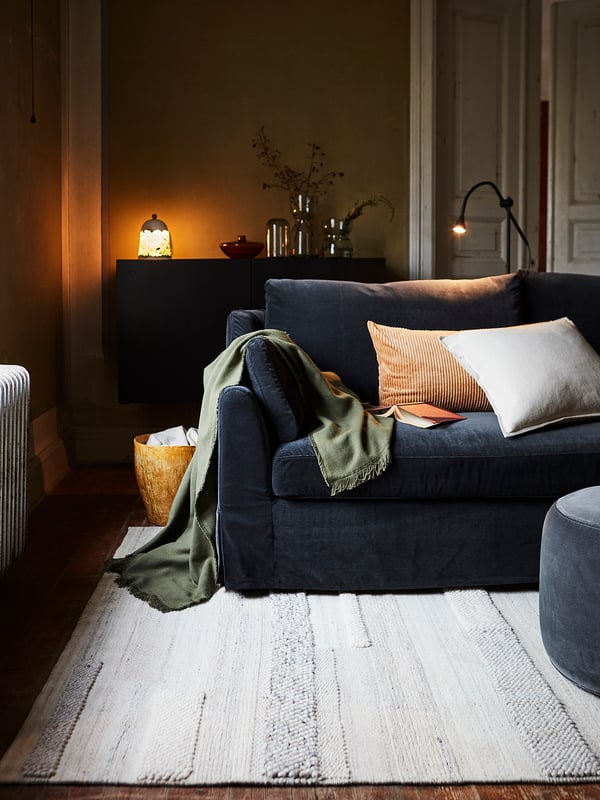 Cosy living room with dark blue BRÖNDEN rug, featuring various weaves and textures, placed under soft lighting.