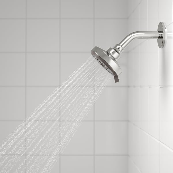 A modern showerhead delivers a powerful, full spray of water against white tiles, showcasing its relaxing and invigorating capabilities.
