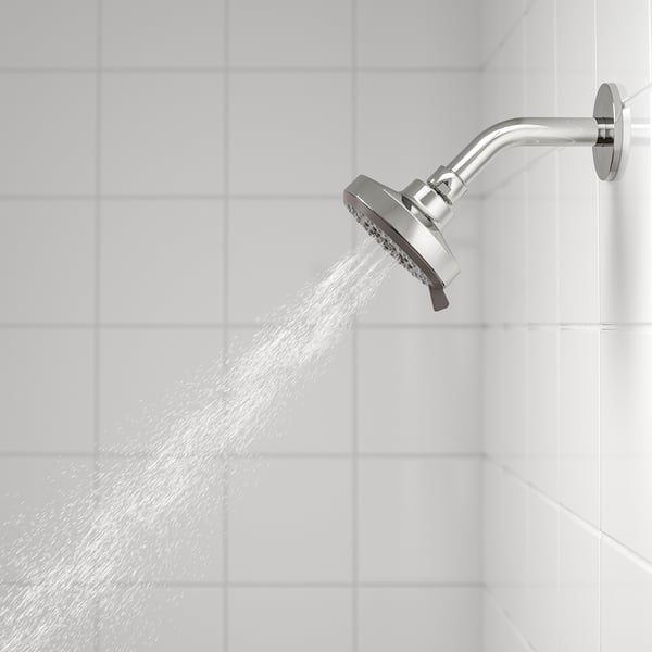 Silver showerhead mounted on wall, spraying water in full, wide setting.