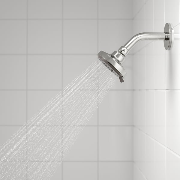 Chrome shower head spraying water on white tiled wall, mounted on adjustable arm.