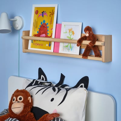 DJUNGELSKOG orange toy monkey, hanging shelf with art, zebra pillow on bed, blue wall.