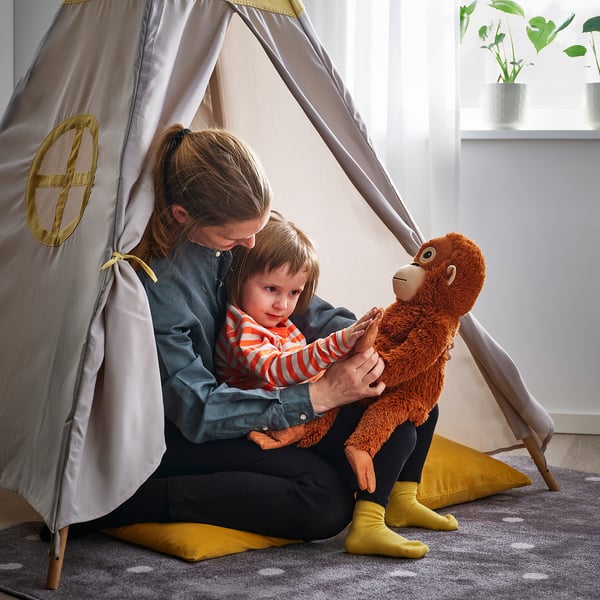 Person and child play indoors with soft toy monkey. Theyre inside a tent, child holds the toy.