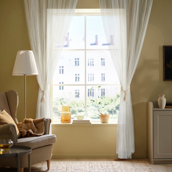 Living room with large window, white curtains, armchair, lamp, rug, cabinet, vase, picture.