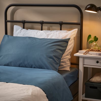 Cosy bed with blue sheets, striped pillows, & plant on bedside table.