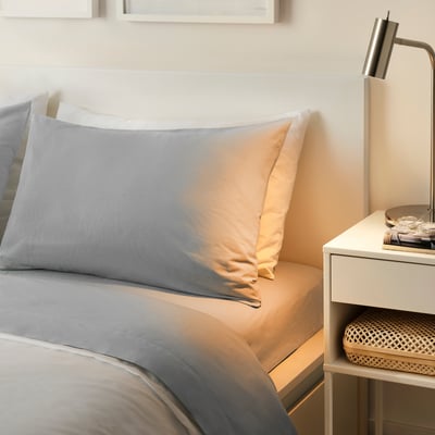 A DVALA grey cotton bed set on a white bed, with a minimalist, cosy look.