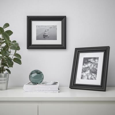 Picture frames on wall and shelf. One frame holds a boat photo, another a butterfly. Shelf holds books, plant, and decorative orb.