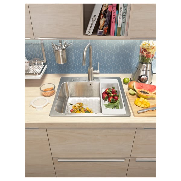 Modern kitchen scene: stainless sink, fruit, blender, wooden cabinets, blue tiled backsplash.