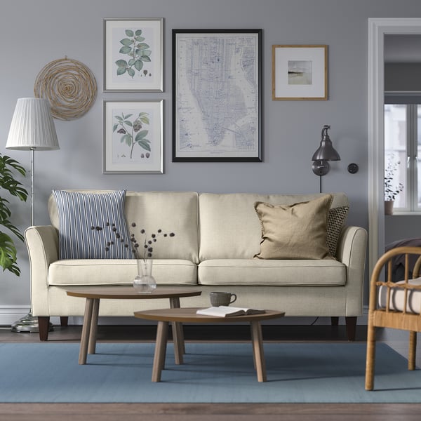 Modern living room: cream EKHOLMA sofa, blue rug, wooden coffee table, wall art, plants, lamp.