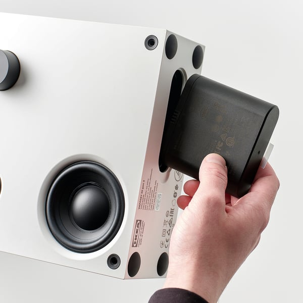 A hand places a black battery into a white speaker. Action shot of ENEBY speaker battery setup.