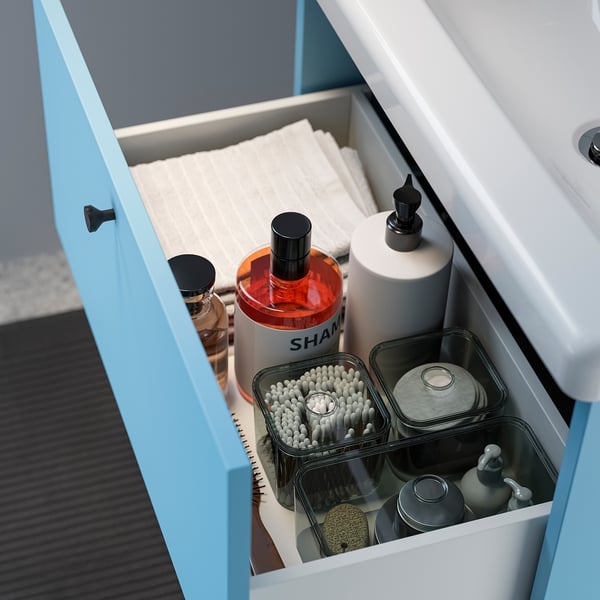Open blue bathroom drawer showing organised toiletries: towels, shampoo, soap, and brushes in containers.