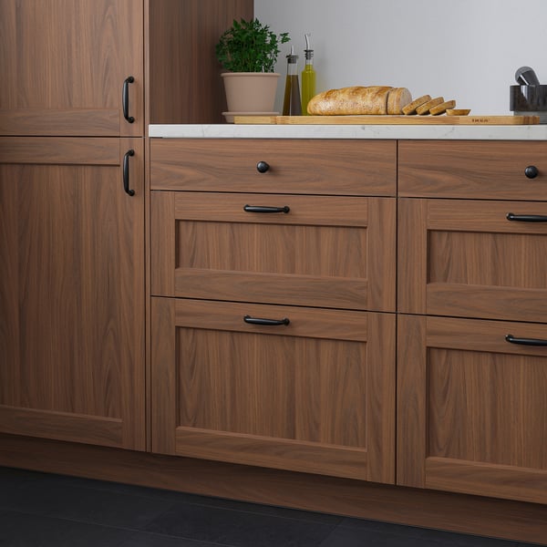 Modern kitchen with tall brown wood cabinets, black handles. Marble countertop with bread, herbs, and oils; looking sleek and organised.
