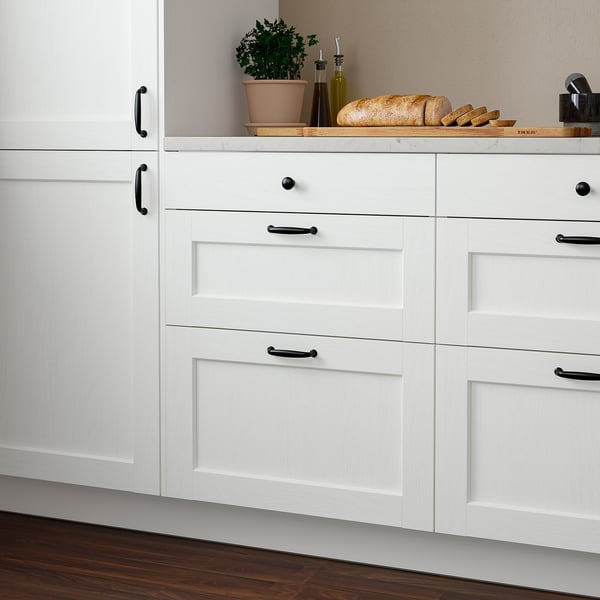 White kitchen drawers, ENKÖPING, simple design, dark handles, small decorative items on top.