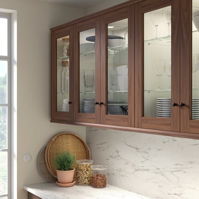 Modern kitchen with brown ENKÖPING glass-doored cabinets above marble countertop. Small jars and plant below.