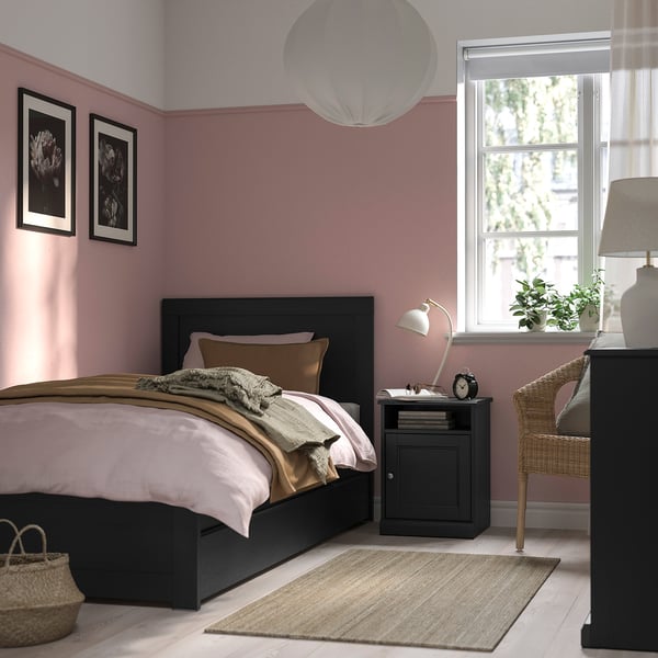 Cosy pink bedroom with FÅGELFJÄLLET black bed, white lamp, and wicker chair.