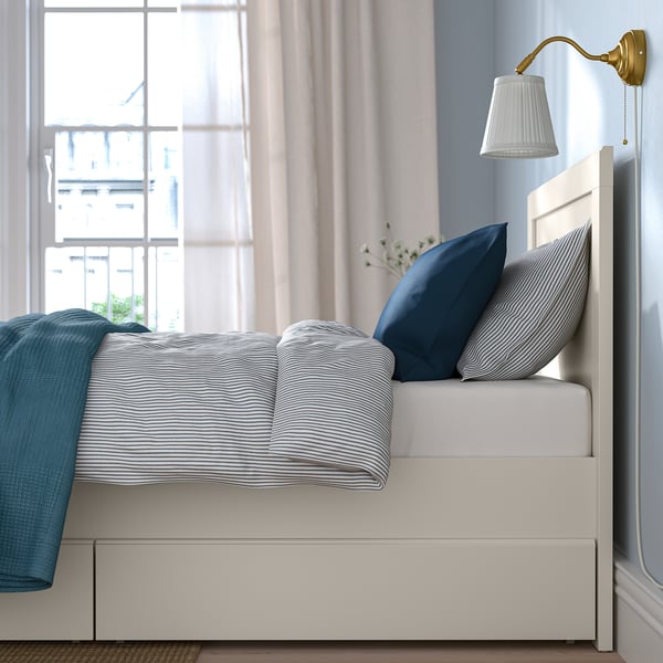 Bedroom scene with white FÅGELFJÄLLET bed, blue bedding, and wall-mounted light.