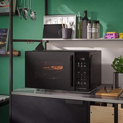 Black GÅTEBO microwave oven with digital display and air fry tray, small & sleek, sits among kitchen items on counter.