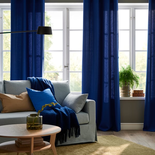 Modern living room with dark blue curtains, wooden coffee table, grey sofa, and green plant.