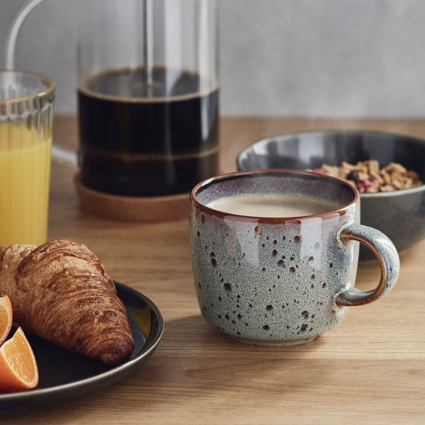 Wooden table set with breakfast items: orange juice, croissant, granola, and coffee in a GLADELIG mug.