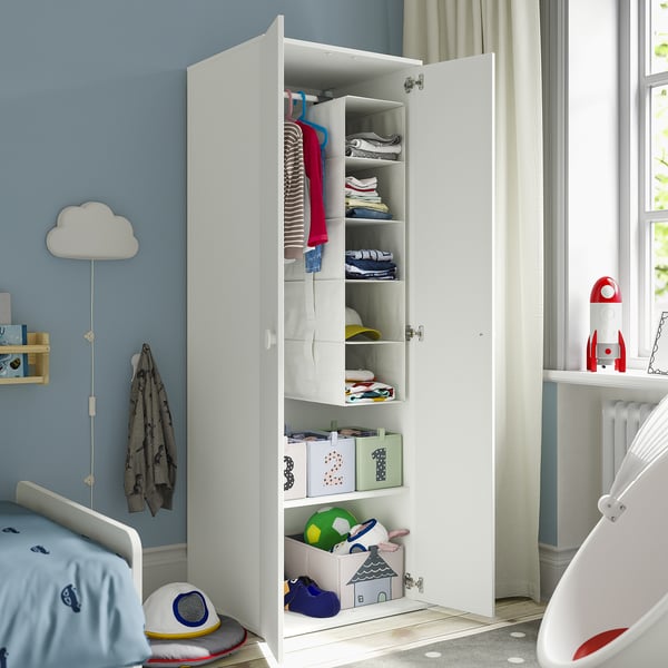 Childs bedroom with open white wardrobe showing shelves, clothes, and toys inside.